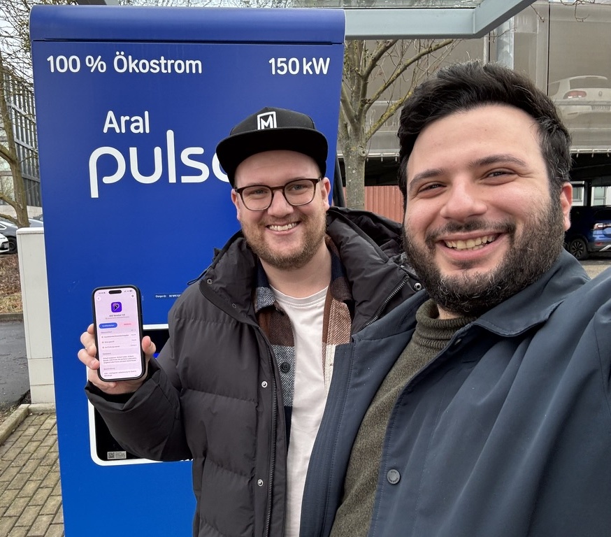 The two friends together at an Aral pulse charging station, holding the phone app